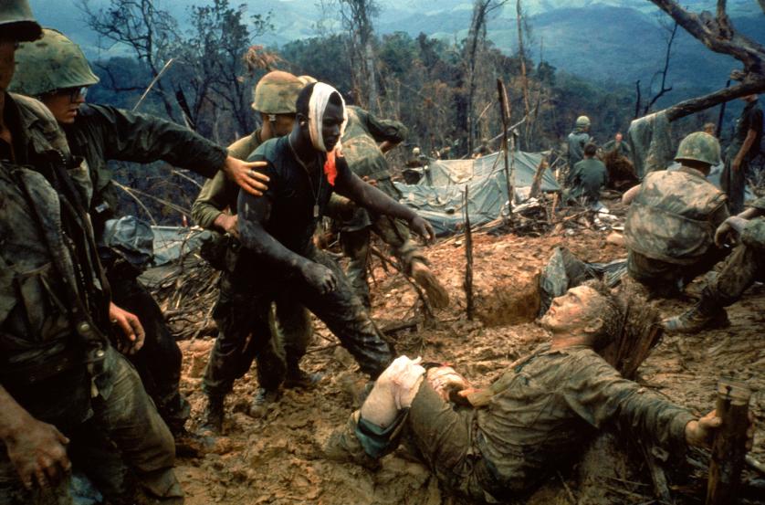 Wounded Marine Gunnery Sgt. Jeremiah Purdie (center, with bandaged head) reaches toward a stricken comrade after a fierce firefight south of the DMZ, Vietnam, October 1966.