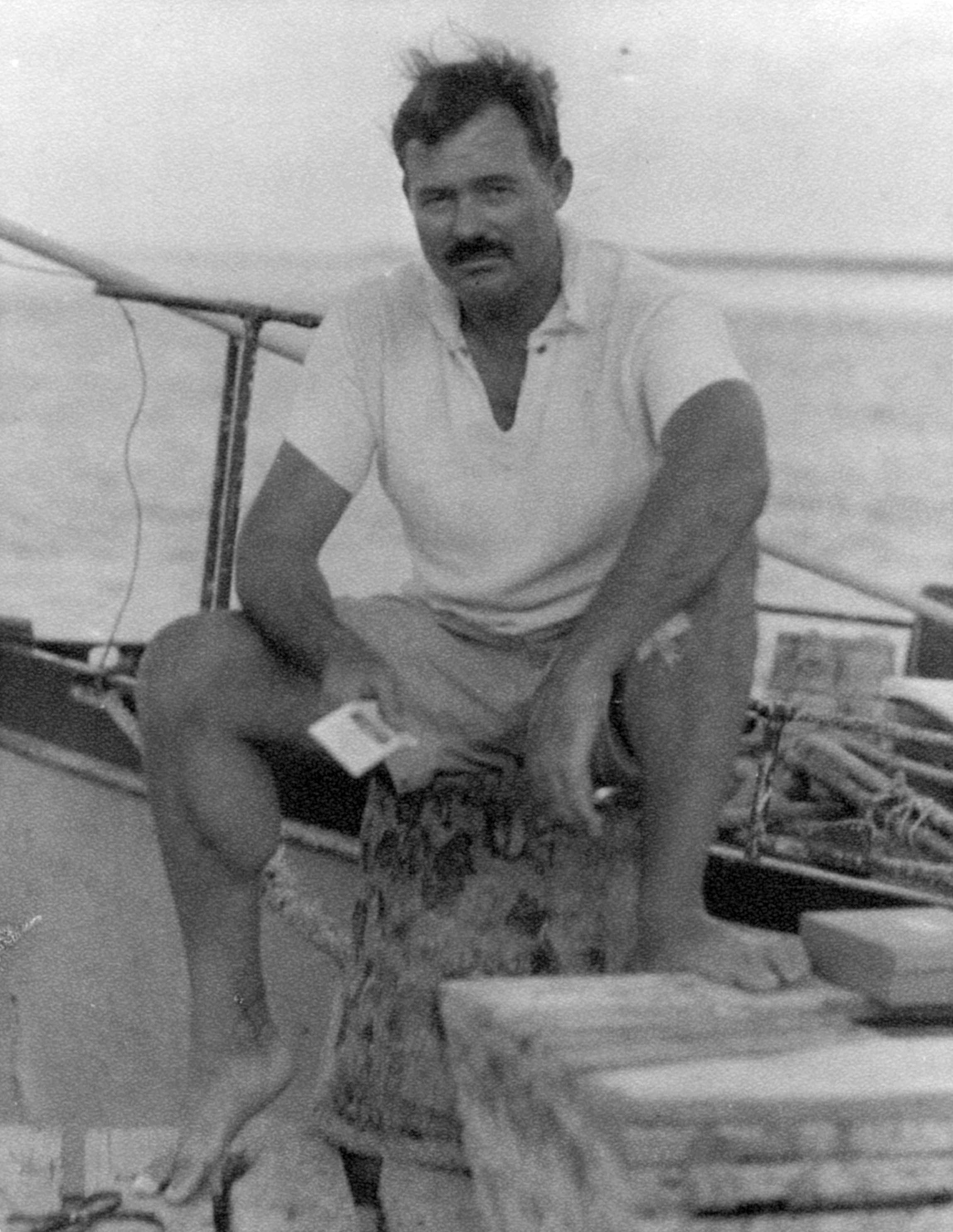 EH6670P   1930s Ernest Hemingway sitting on a dock next to the Pilar, 1930s.  Photographer unknown in the Ernest Hemingway Collection of the John F. Kennedy Presidential Library and Museum, Boston.